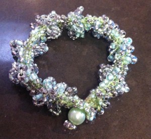 A small bracelet in which a mixture of pale green and clear silver-lined beads is crocheted into blue-green embroidery cotton. Finished with a beaded loop and a large green bead closure.