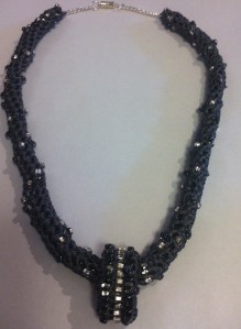 Grey tape/ribbon crocheted with a spiral pattern of dark grey and clear beads. Loop pendant. 